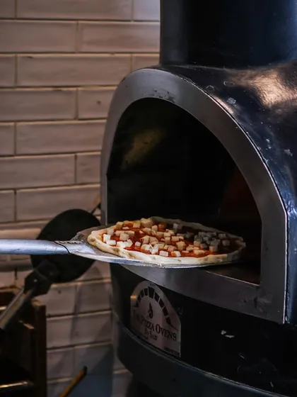 Pizza in progress. A pie topped with cheese cubes is ready to slide into the fiery oven. This is the moment before the transformation begins.