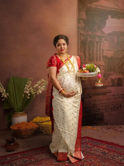 A full-length portrait showcasing a traditional Bengali look. The mother-to-be holds a tray of offerings, set against a backdrop reminiscent of a temple, celebrating cultural rituals.