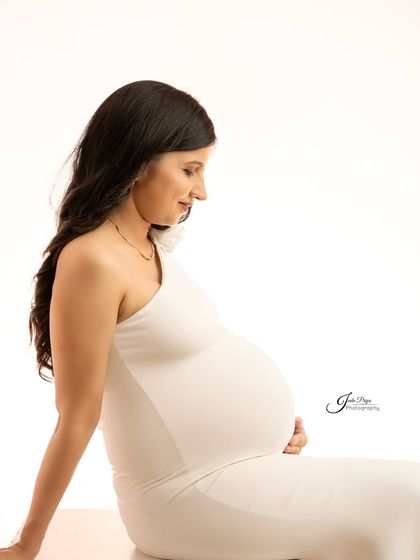 A simple, profile view of the mom-to-be in a fitted white gown. This pose beautifully highlights the curve of her baby bump against a clean white background.
