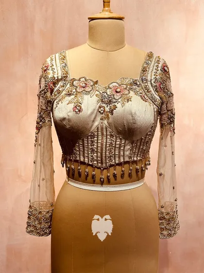 For the modern bride, I create contemporary heirlooms. This corset-style blouse in soft beige raw silk features delicate floral embroidery and sheer georgette sleeves. It’s a vision of quiet elegance, balancing modern femininity with timeless craftsmanship.