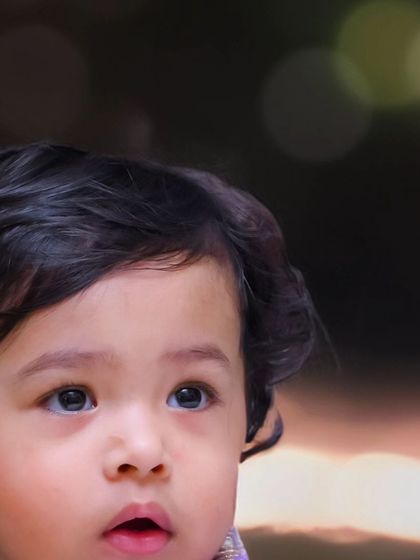 A close-up portrait of a baby looking up in wonder. The soft, out-of-focus background lights create a magical bokeh effect, drawing all attention to the child's innocent expression.