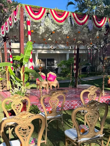A traditional Brahmin wedding mandap setup in a garden. The vibrant colors, ornate chairs, and surrounding greenery create a festive and sacred atmosphere.