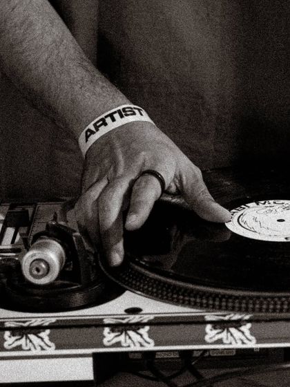 A close-up of my hand on the vinyl, wearing the artist wristband. This shot captures the tactile nature of DJing with records, a craft I am deeply passionate about.