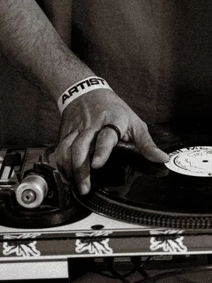 A close-up shot of a hand on a vinyl record, with an 'ARTIST' wristband visible. This image captures the essence of being a selector at one of my all-vinyl events.