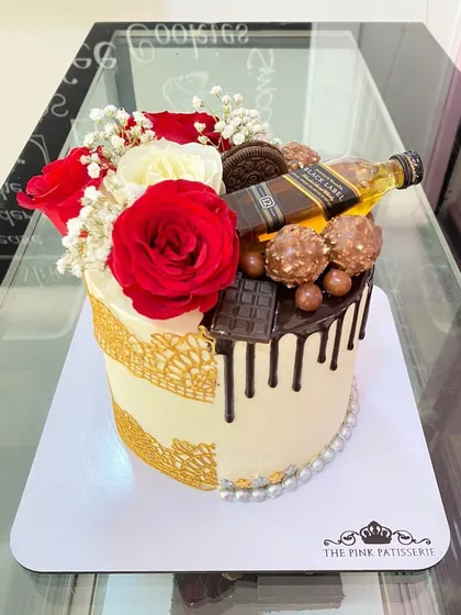 A unique half-and-half cake. One side is elegant with red roses and gold lace, while the other is a decadent chocolate drip cake topped with a miniature Black Label bottle.