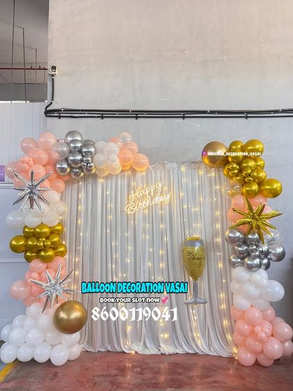 A beautiful balloon arch against a curtain with fairy lights. The peach, white, silver, and gold balloons create a warm and celebratory feel.