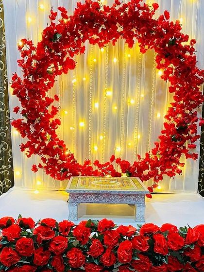 A beautiful circular frame of red flowers set against a white curtain with pearl strings and fairy lights. This setup is ready for your idol, providing a vibrant and glowing backdrop.