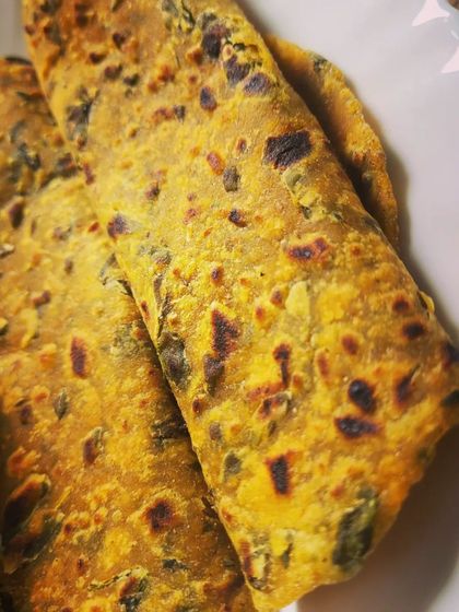 A close-up of the Methi Parathas, showing the specks of green fenugreek leaves and the perfectly cooked, flaky texture.