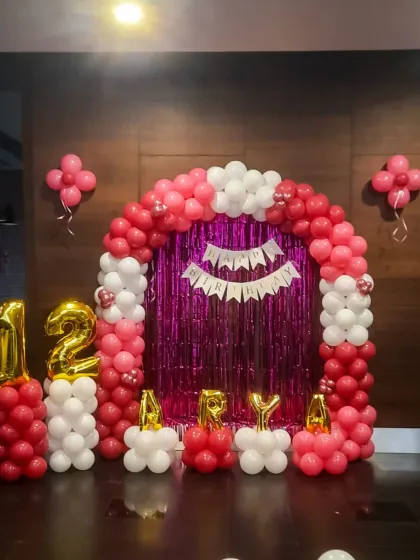 This balloon arch in shades of pink and white was for a 12th birthday. The setup includes large gold foil numbers and a 'Happy Birthday' banner against a magenta tinsel curtain, creating a vibrant and fun photo area.