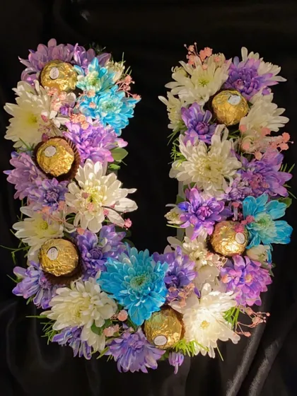 A full view of the custom 'U' monogram bouquet against a dark backdrop, making the bright colors of the chrysanthemums and the gold of the Ferrero Rocher pop.