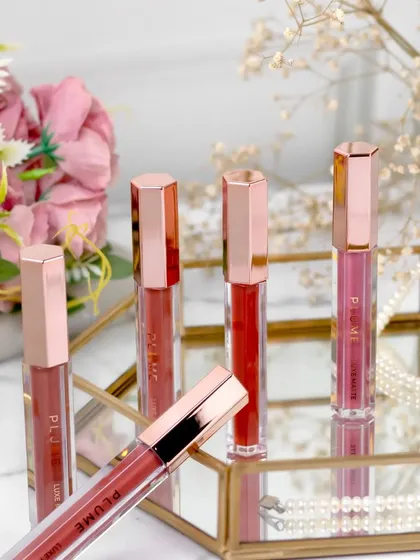 These liquid lipsticks are elegantly displayed in a mirrored gold tray, with soft florals in the background. The reflection adds a touch of glamour, while the pearls suggest luxury and sophistication.