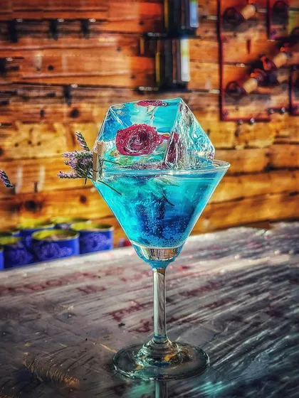 We believe drinks should be a work of art. This cocktail features a custom-made ice block with a rose frozen inside, showing how we use infused ice and unique garnishes to elevate your drink menu.