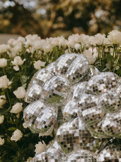 A cluster of disco balls nestled among a bed of white roses, adding a touch of modern glam to the romantic floral decor.