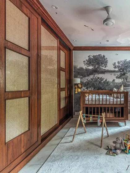 This wide shot shows the custom wood and cane sliding wardrobe, which provides a warm, natural texture to the room. The soft rug and wooden play gym make the floor a safe and comfortable play area.