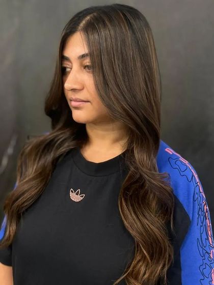 A side profile of the client, her balayage hair styled into soft, face-framing waves.