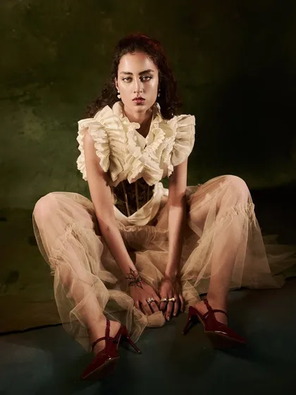This image captures a powerful, direct pose from the 'Velvet Shadows' series. The broad lighting setup illuminates the entire scene, showing off the full outfit, the intricate details of the ruffled top, and the model's confident presence.