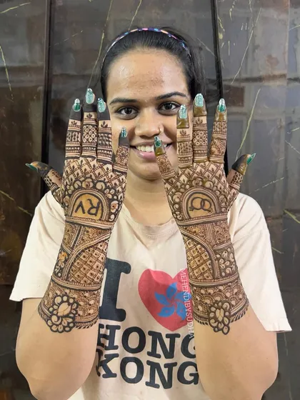 A happy bride-to-be showing her engagement mehendi, personalized with initials 'R' and 'V'.