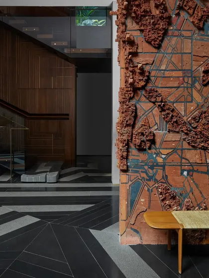 A large-scale terracotta wall art installation by artist Pravat M at the Baid Residence. This piece explores urban landscapes and architectural forms, adding a raw, textural element that contrasts with the polished granite floors.
