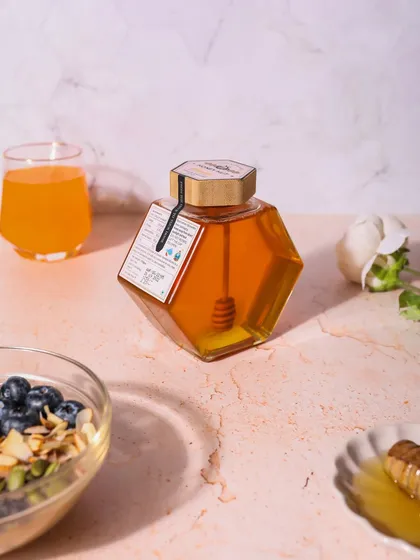 A beautiful shot of a unique hexagonal honey jar. The styling with a breakfast bowl and juice suggests a healthy and delicious way to start the day.