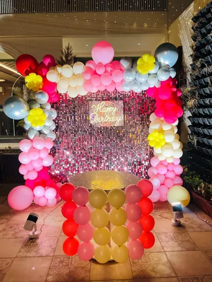 A bright and cheerful birthday backdrop with a pink sequin wall and a multi-colored balloon frame.
