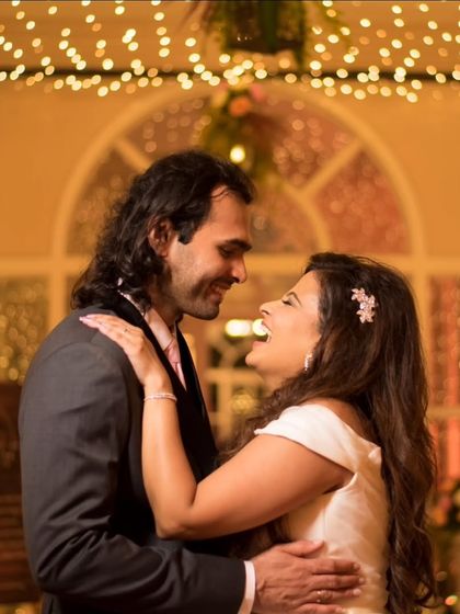 A candid moment of shared laughter between the bride and groom, captured against a backdrop of warm fairy lights.