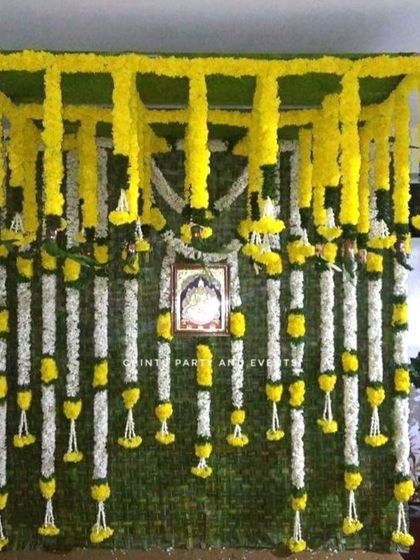 A Half Saree function decoration with a backdrop of woven banana leaves. The setup is decorated with garlands of yellow and white flowers.