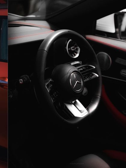 An interior shot focusing on the Mercedes-AMG steering wheel and cockpit. The dark, moody lighting creates a sophisticated atmosphere, drawing attention to the driver-focused design and luxury materials.