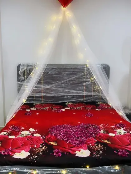 A close-up of the bed from the romantic room setup, showing the simple canopy created with fairy lights and a bedspread covered in rose petals.