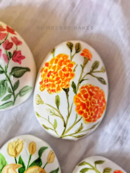 A close-up of a marzipan egg with a hand-painted marigold flower design.