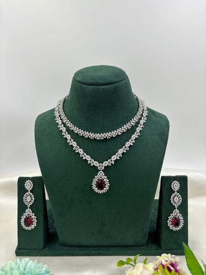A graceful double-layered AD necklace. The top layer is a simple floral chain, while the bottom layer features a pear-shaped pendant. It is available in white, pink, green, and blue stones.