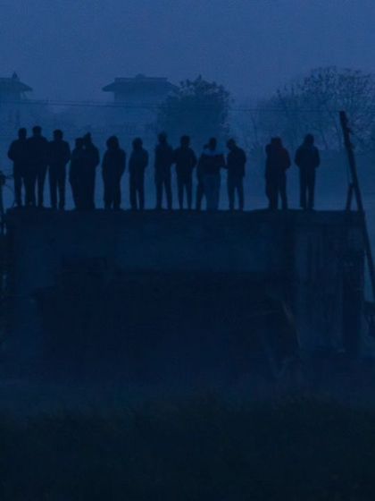 Villagers watch from a rooftop in the pre-dawn fog, their silhouettes standing vigil as the historic rescue operation unfolds.