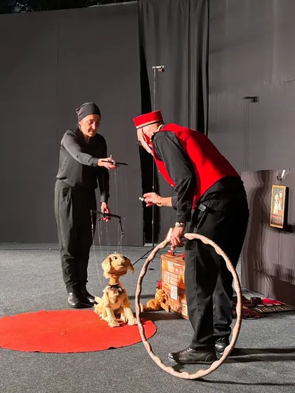 Another angle of the dog training scene from 'Pay Attention to Those Two', highlighting the dynamic interaction between the puppeteers and the marionette.
