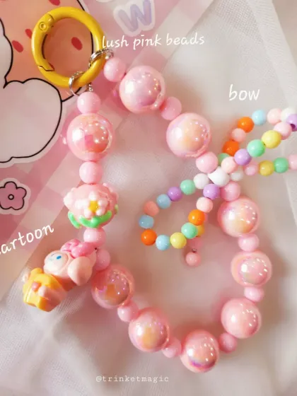 This pink beaded bag charm is full of cute details, including lush pink beads, cartoon character charms, and a smaller strand of rainbow beads for extra fun.