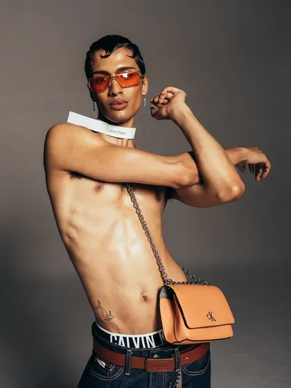 A dynamic studio portrait for a Calvin Klein campaign. The composition highlights the model's physique and the brand's accessories, blending classic fashion photography with a modern, energetic feel.