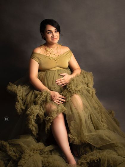 A regal portrait of a mother-to-be seated in an olive green ruffled gown, looking thoughtfully to the side.