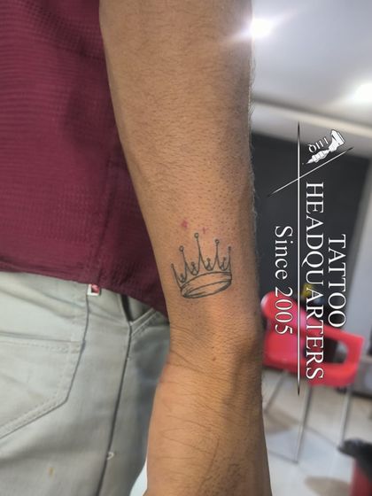 A small, simple crown outline tattoo on the wrist, symbolizing self-control and sovereignty.