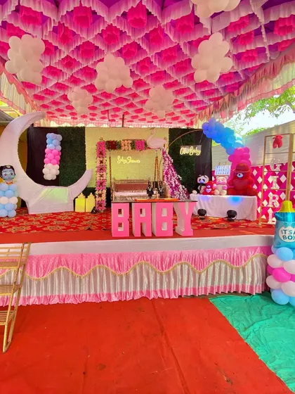 A full view of a baby shower stage with a moon prop, decorated swing, and balloon clouds hanging from the ceiling.