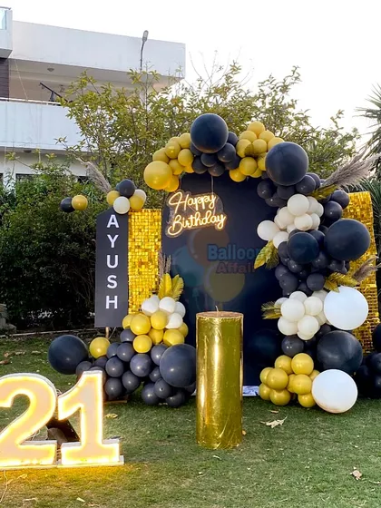 A stylish 21st birthday party in a garden with a black and gold theme, featuring a shimmer wall and marquee numbers.