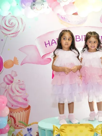 The adorable birthday twins, Eishana and Rianna, in front of their sweet-themed backdrop. Their matching dresses complete this picture-perfect moment.