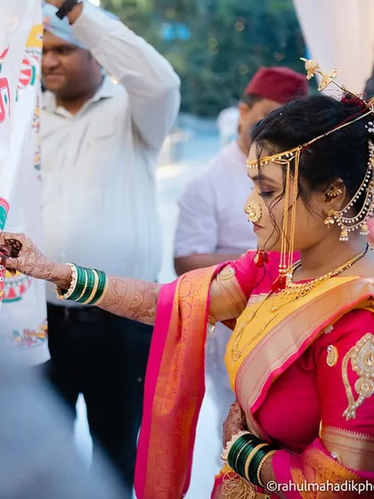 The bride performing a wedding ritual, her profile highlighting the traditional Maharashtrian jewelry and hairstyle.