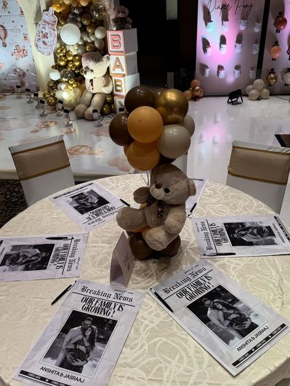 A creative table setup featuring a teddy bear centerpiece and custom 'Breaking News' flyers announcing the family's growth. It's these small, personalized details that make a celebration unique.