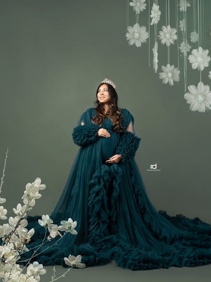 A regal portrait of a mom-to-be wearing a crown. The dramatic green gown and floral accents create a look that is both powerful and beautiful.