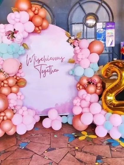 A fun 'Mischievous Together' anniversary or couple's party setup with a custom backdrop and balloon garland.