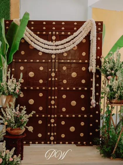 A traditional wooden door with brass accents, decorated with jasmine garlands, serving as a stunning photo backdrop or entrance element.