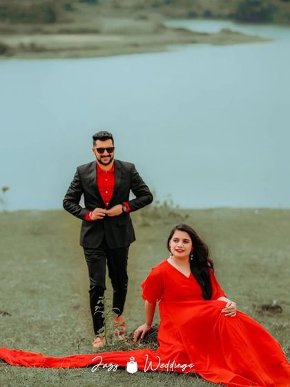 A stylish and modern pre-wedding photo by the water. The couple has coordinated with matching red shirts, with the partner adding a sharp black blazer.