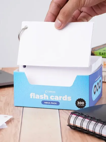 A lifestyle shot of flash cards on a desk with a laptop and books. A hand reaching for a card demonstrates the product's use in a study or work environment, highlighting its practicality.