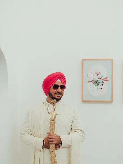 A cool and modern groom portrait. Dressed in a classic white sherwani and stylish sunglasses, he holds his kirpan, blending tradition with contemporary flair.