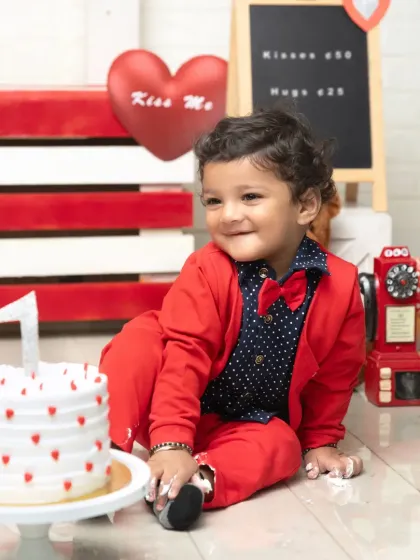 A sweet smile before the cake gets smashed. The "Kisses & Hugs" sign adds a charming touch to this adorable Valentine's first birthday setup.