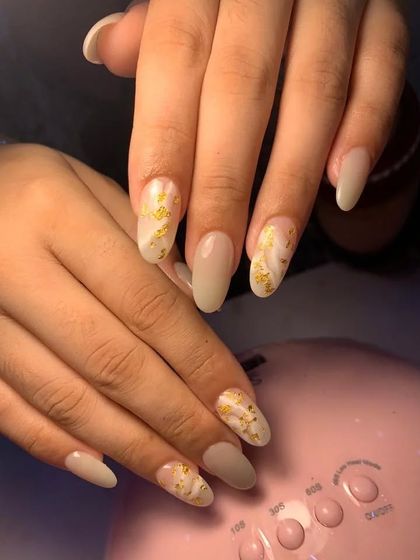 An elegant set of almond-shaped nails with a milky white base and delicate gold foil accents.
