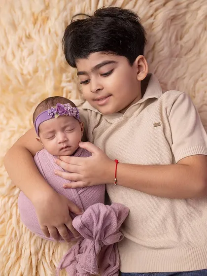 A close-up of the sibling bond, with the brother gently holding his swaddled sister.